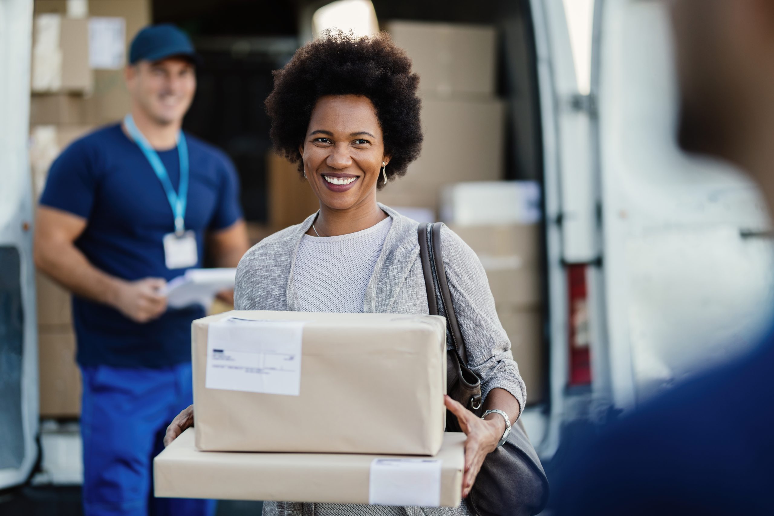Happy African American woman holding delivered packages. A couriers is standing in the background.